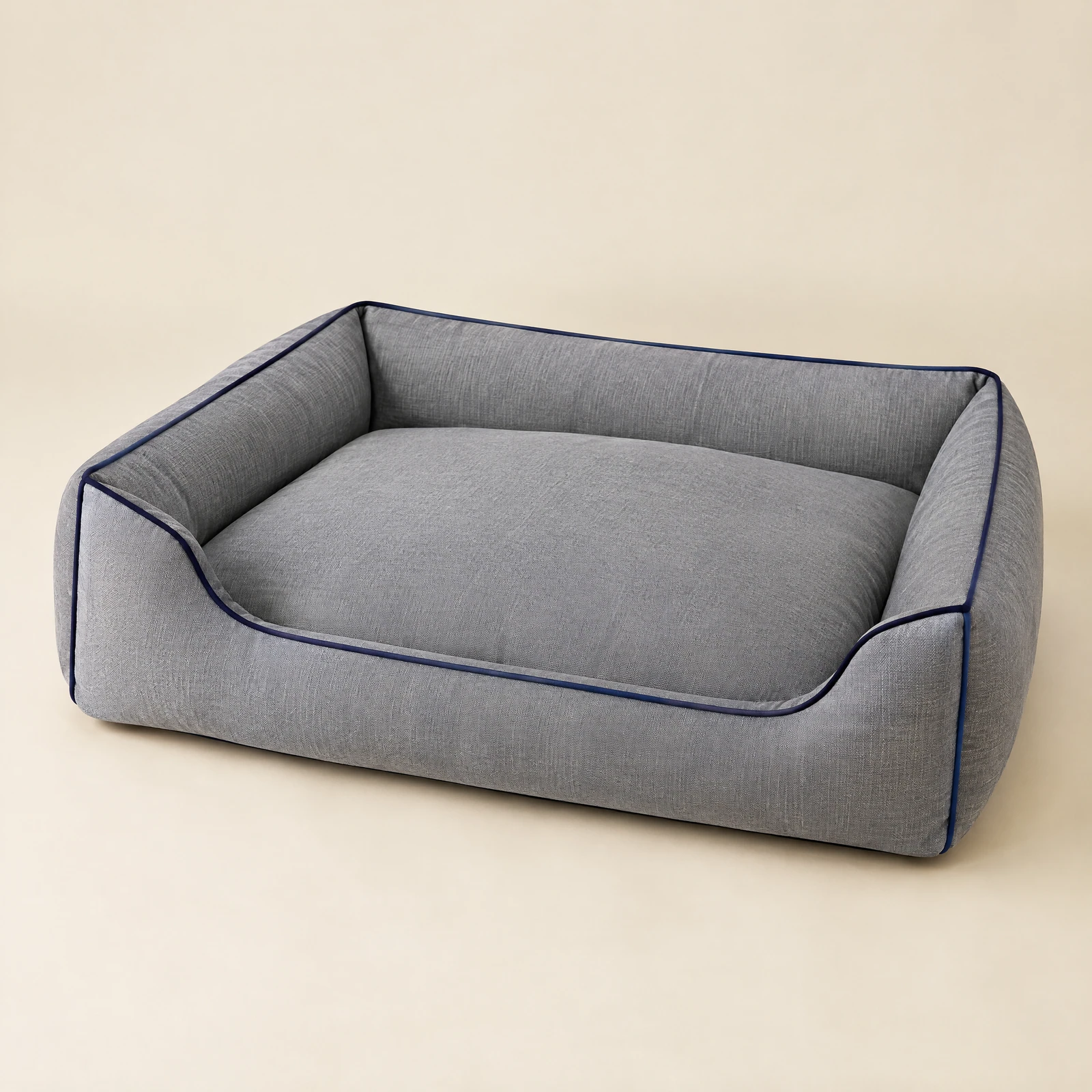 A rectangular gray dog bed with navy piping, empty, shown at a slight angle on a cream background