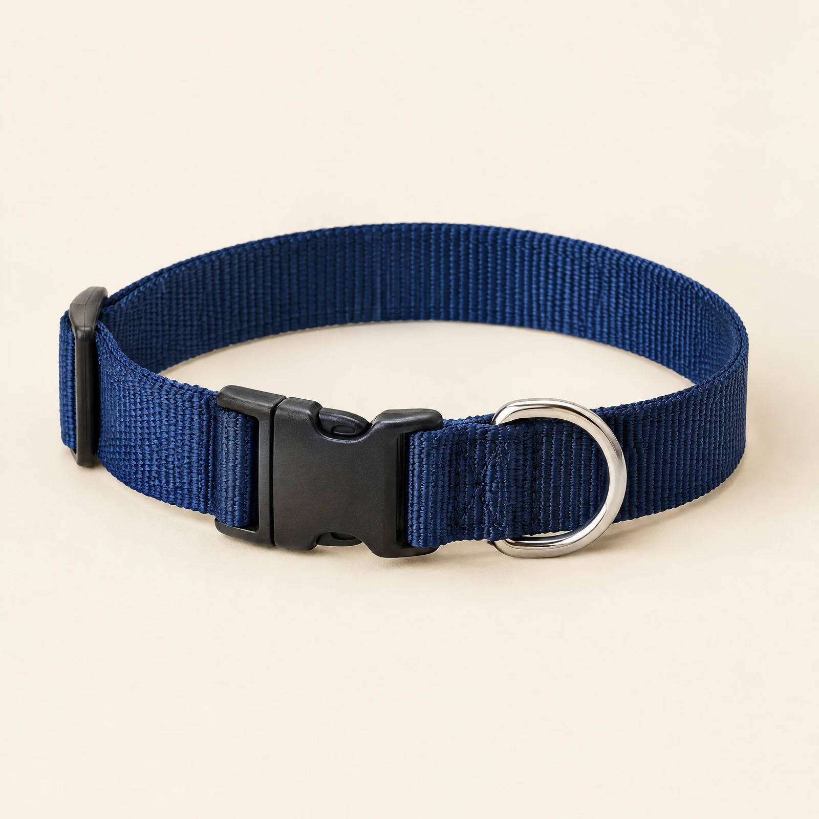 A navy dog collar with a black side-release buckle and a silver-tone D-ring, coiled on a cream background