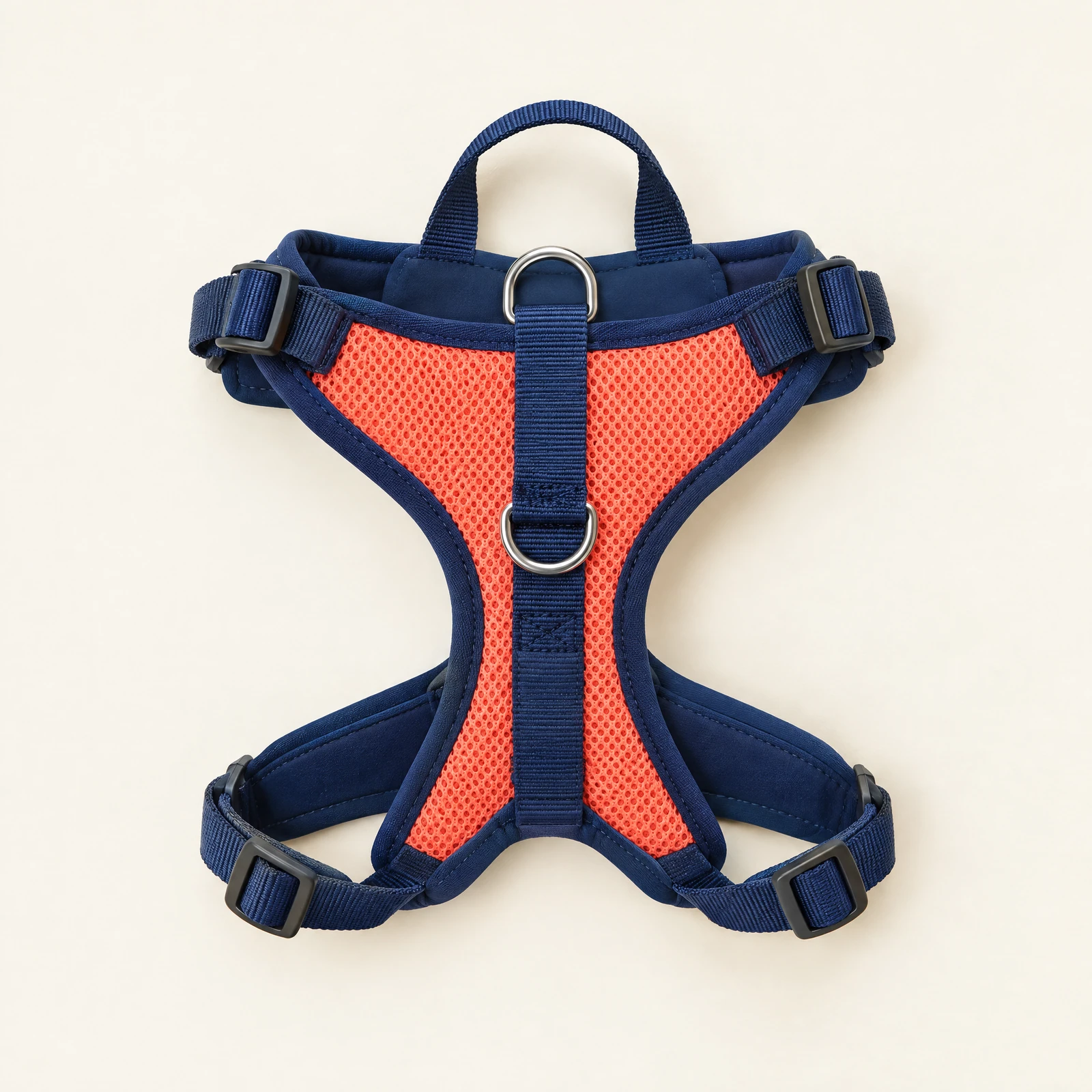 A navy and coral padded dog harness with an open-weave back panel, two silver-tone rings and a top handle, laid flat on a cream background