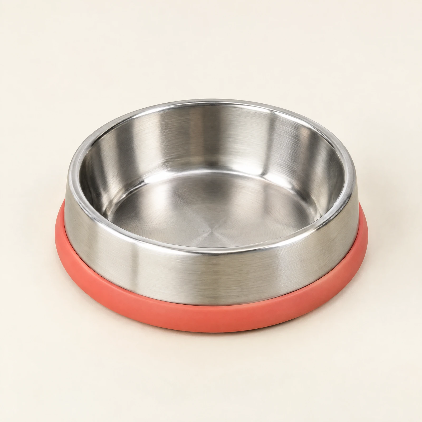 A brushed silver-tone dog bowl with a coral base ring, empty and shown at a slight angle on a cream background